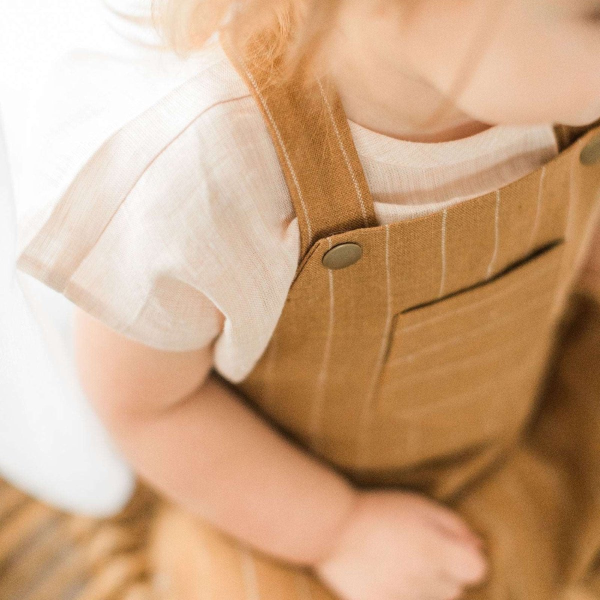 detail view of Beya Made pale pink linen top worn by toddler girl with brown striped overalls